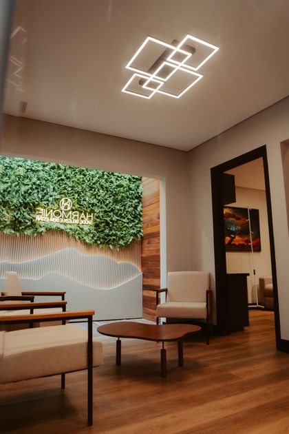 Sala de espera da Harmonie, com poltronas, parede viva e luminária no teto